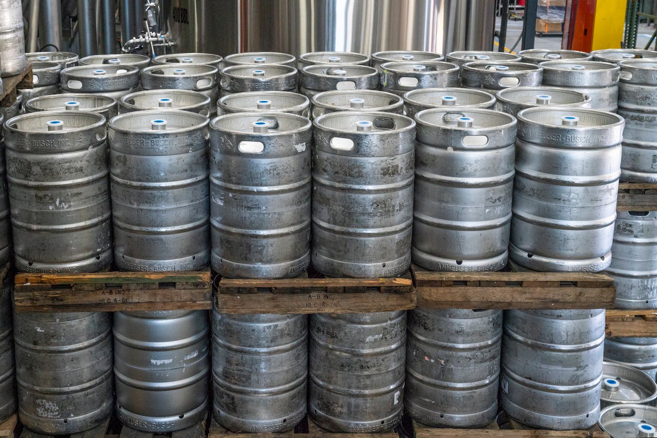 Steel kegs neatly stacked on pallets in an industrial brewery warehouse.